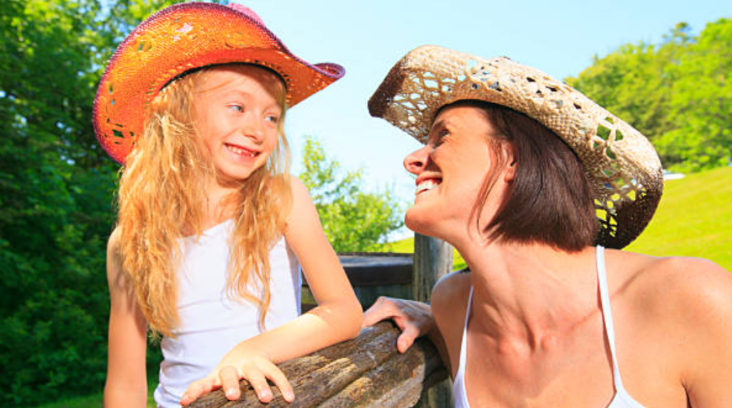 Image mother and daughter wearing cowboy hats, smiling in a field
